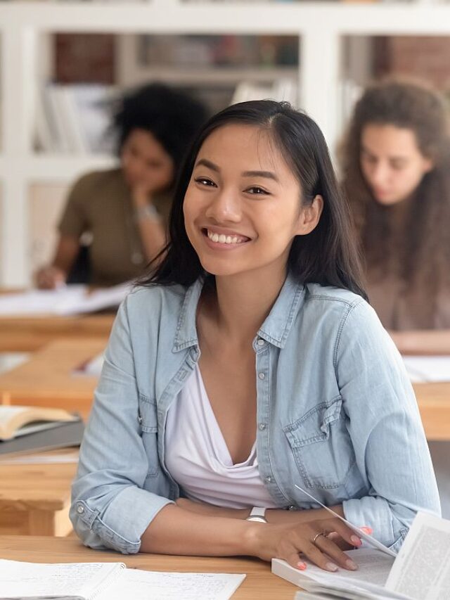 Smiling smart asian student looking at camera sitting at desk